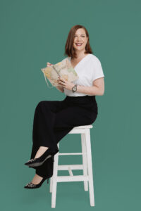 Charlotte Davies smiling and sitting on a stool with a notebook