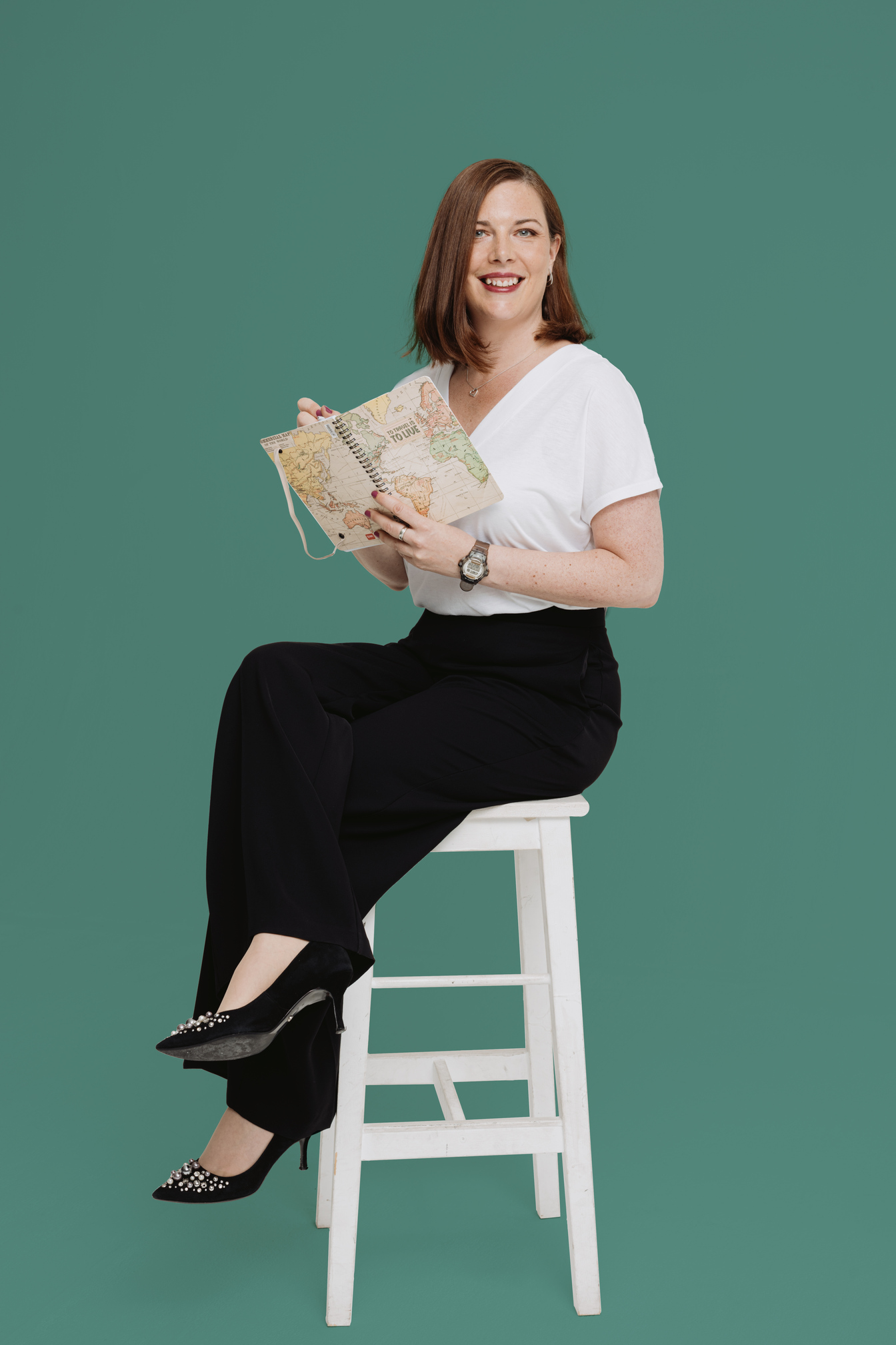 Charlotte Davies smiling and sitting on a stool with a notebook